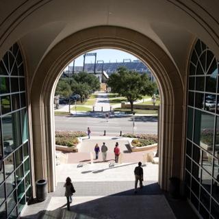 TCU students walk through the University Union arch with the football stadium in the background